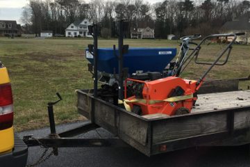 A trailer with mower and spreader in front of a large yard